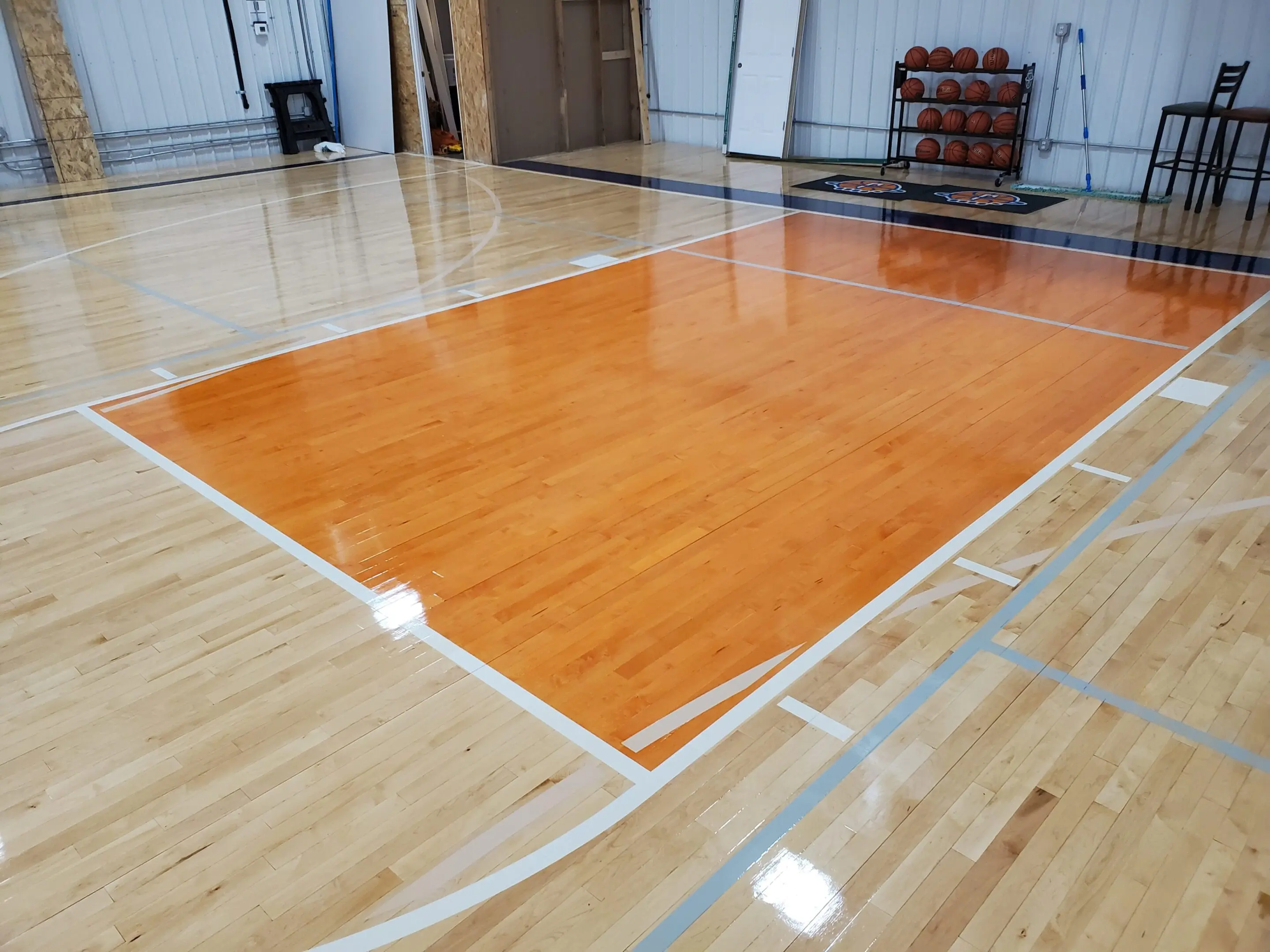 A basketball court with wood flooring and orange colored floor.